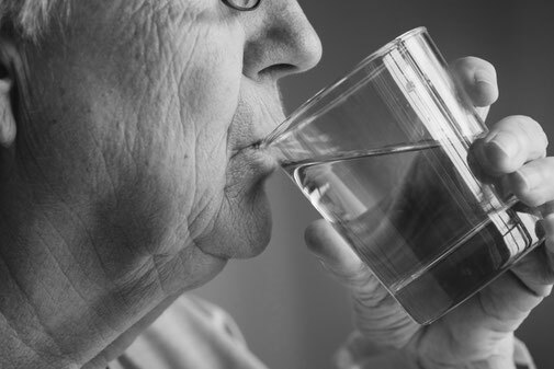 Ältere Person trinkt Wasser aus einem Glas, Nahaufnahme in Schwarz-Weiß.